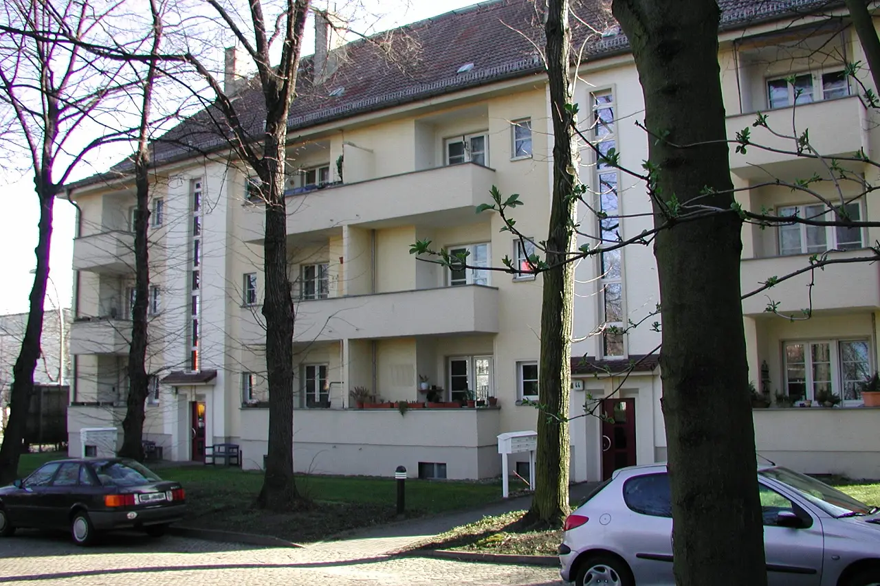 Mehrgeschossiges Wohnhaus mit Balkonen hinter Straßenbäumen in Lichtenberg