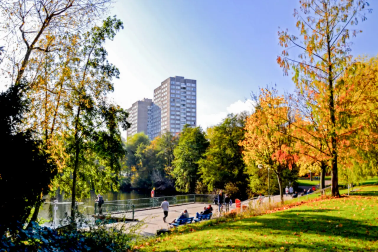 Herbstlicher Park mit Teich und Hochhäusern im Hintergrund in Lichtenberg